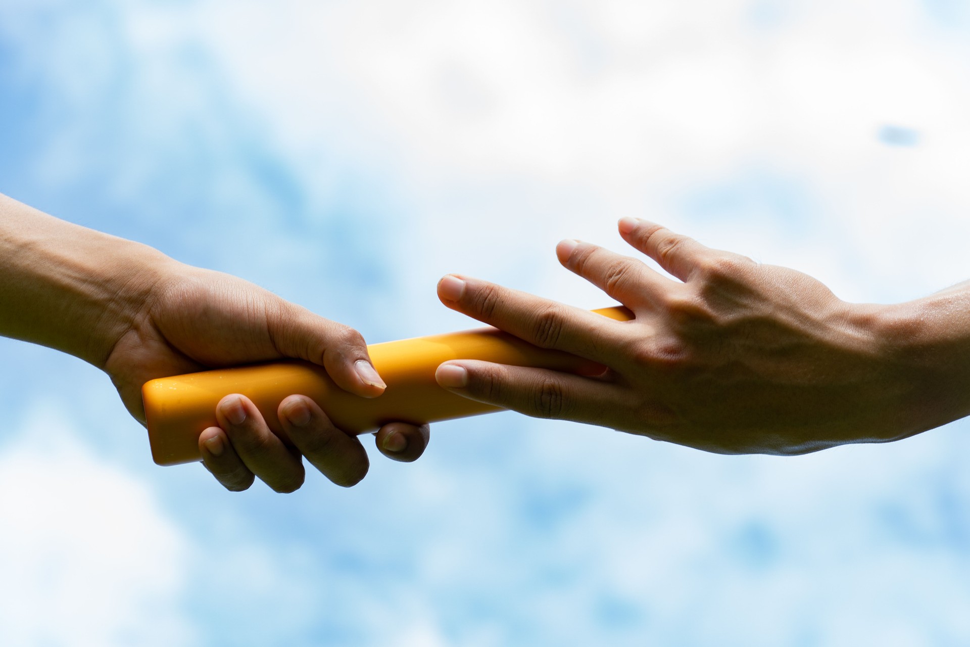 Close up hand set baton from hand to hand on sky background. Business concept for teamwork and team builder.